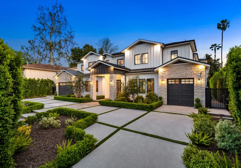 A large white house with a driveway and bushes.